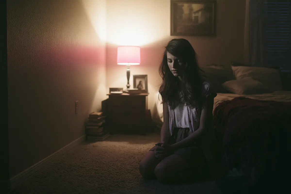 A woman praying quietly at her bedside by candlelight, the way Christian bedtime prayers are meant to be said — unhurried, and not necessarily finished